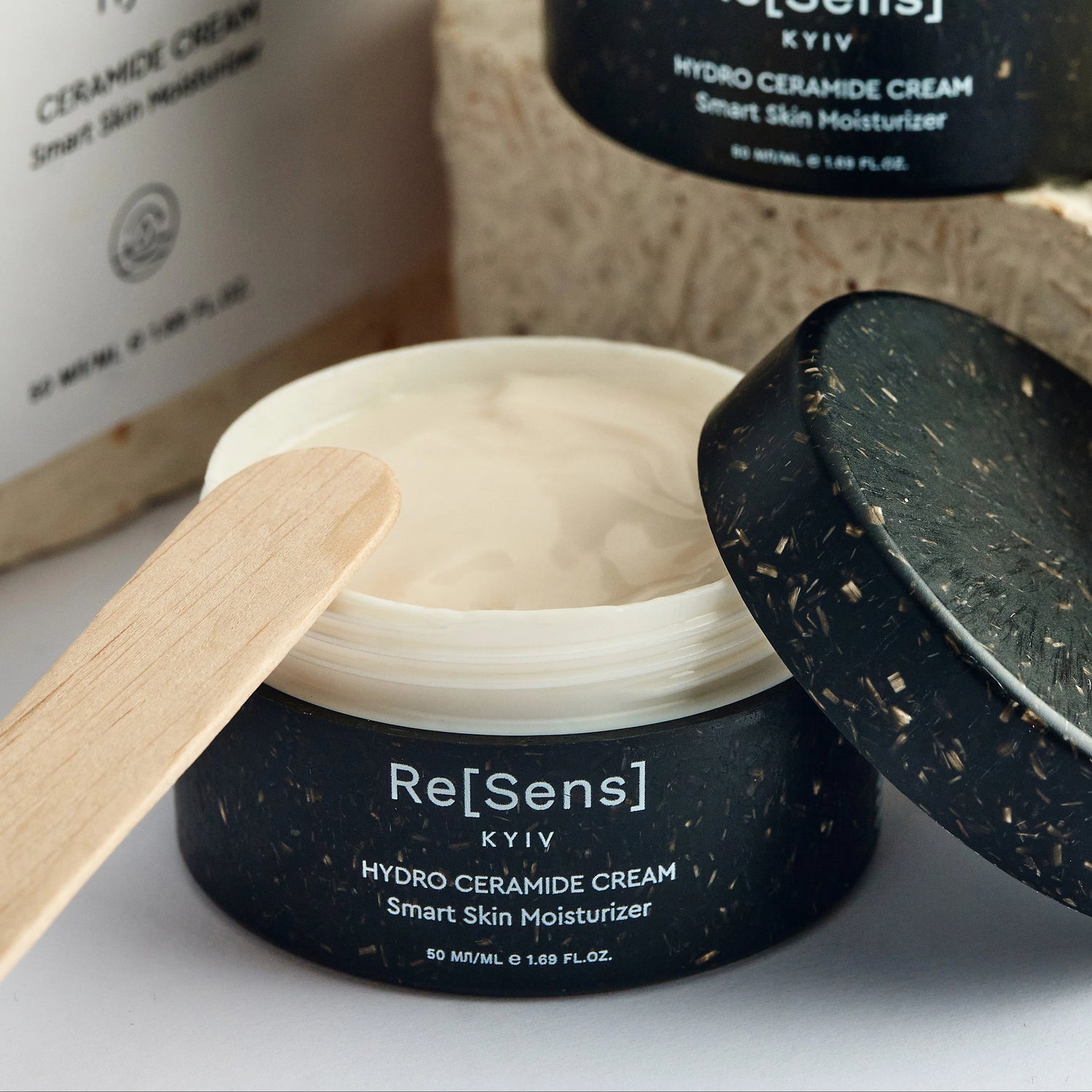 Hydro ceramide cream with a wooden applicator and open lid on a white background